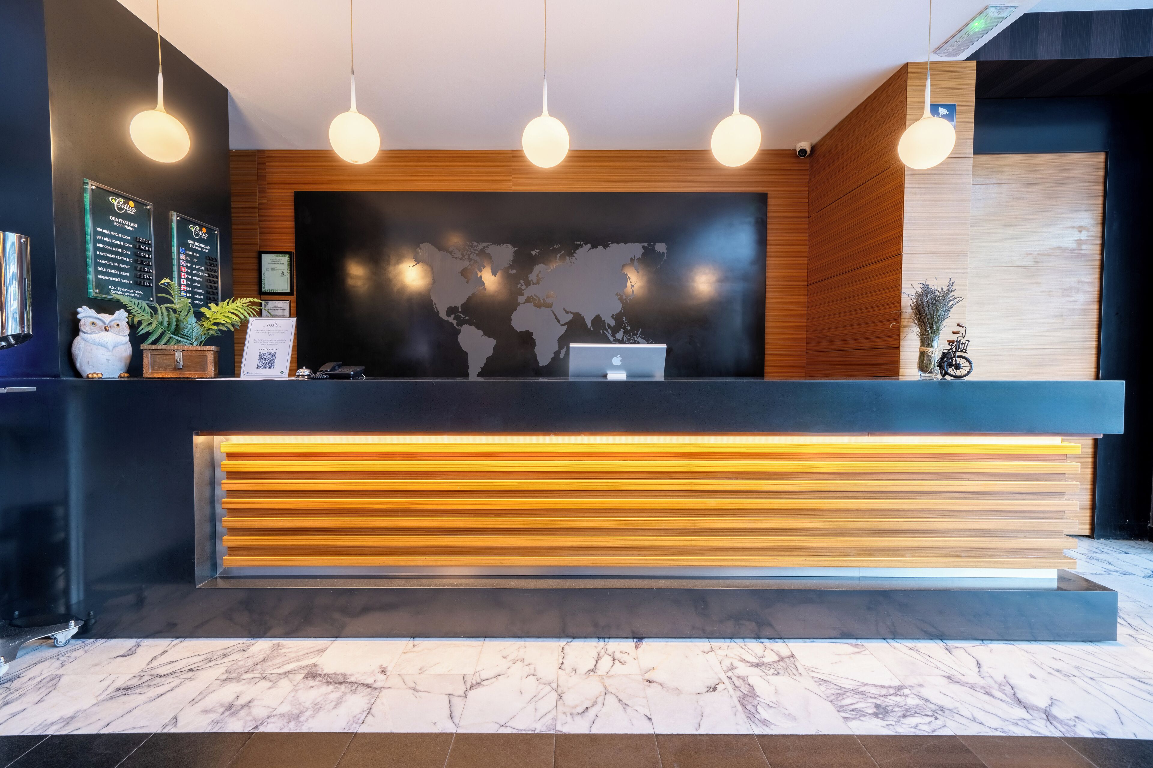 Un mostrador de recepción moderno con un mapa del mundo de fondo, una computadora portátil y una pizarra con el menú.