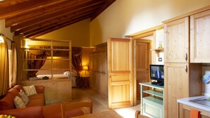 A cozy room with a wooden ceiling, a dining table, a sofa, and a television in a wooden cabinet.