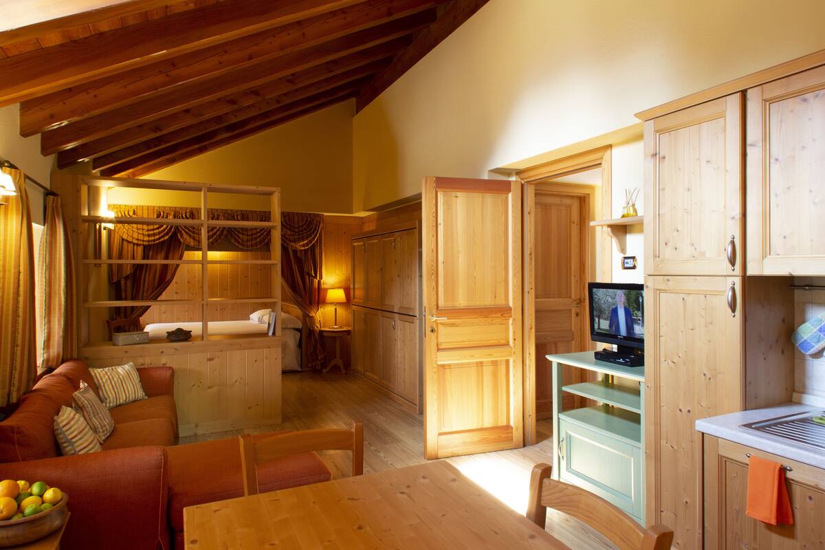 Una habitación acogedora con techo de madera, una mesa de comedor, un sofá y un televisor en un mueble de madera.