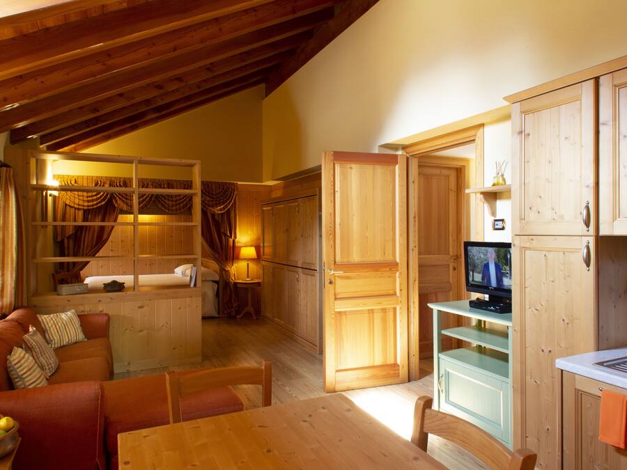 A cozy room with a wooden ceiling, a dining table, a sofa, and a television in a wooden cabinet.