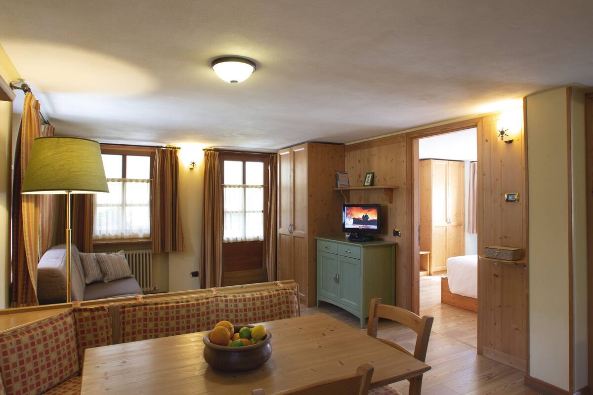 Una habitación acogedora con una mesa de madera, un sofá, un televisor y una ventana con cortinas.