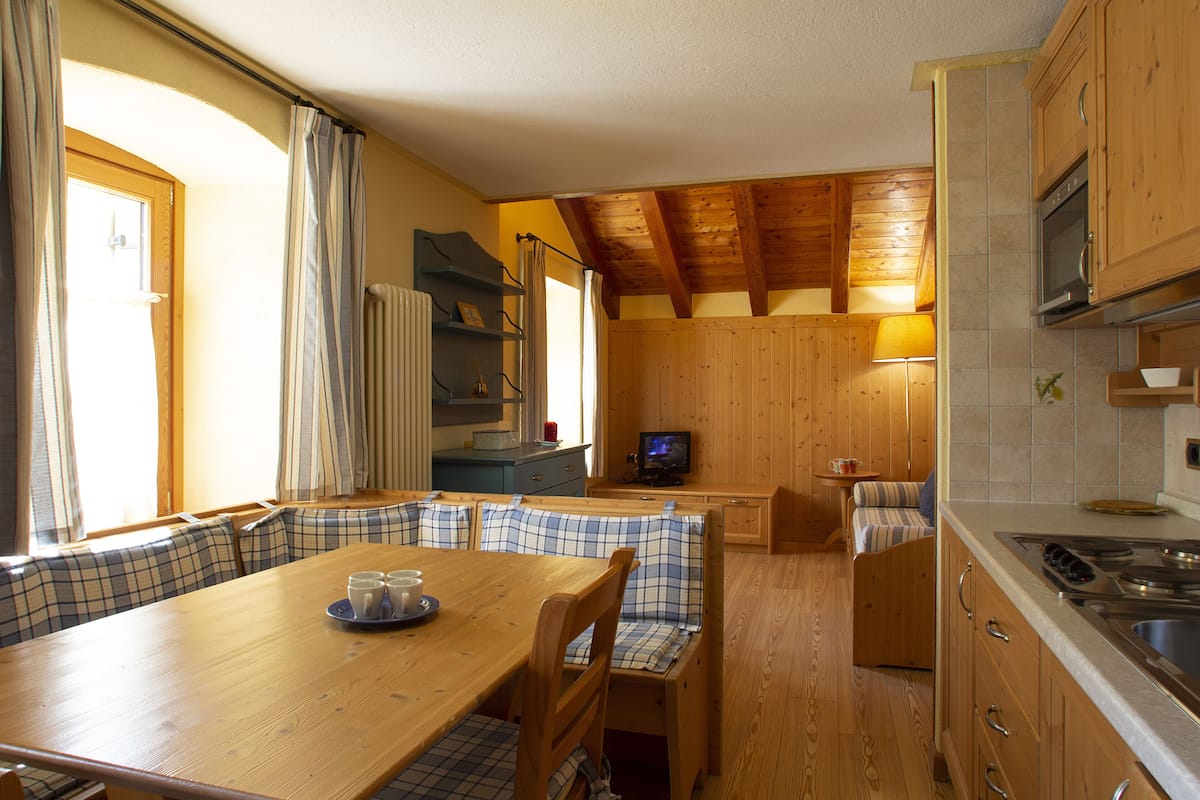 Una cocina acogedora con armarios de madera, una mesa de comedor con mantel a cuadros y un televisor en una esquina.