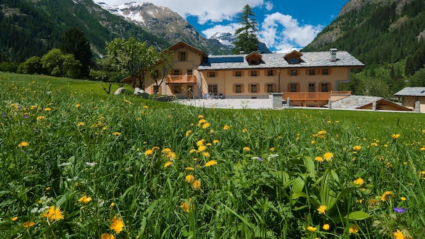 A mountain lodge with a large balcony, surrounded by lush greenery and mountains.