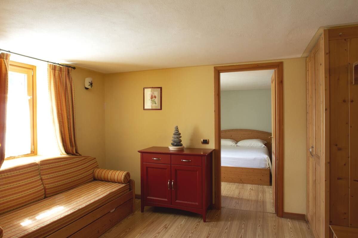 Una habitación con piso de madera, un armario rojo, una cama con cabecera de madera, una ventana con cortinas y un cuadro en la pared.
