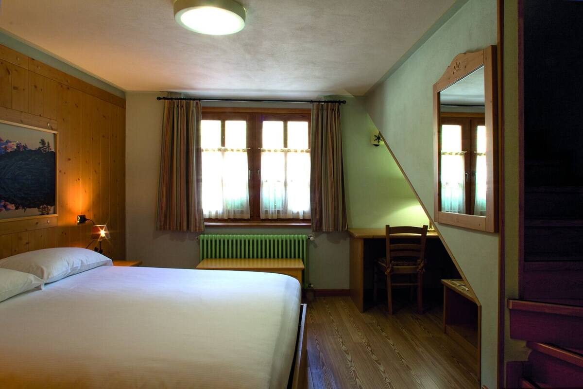 Un dormitorio con cama, escritorio, silla, radiador y ventana con cortinas.