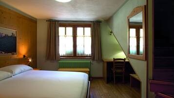 A bedroom with a bed, a desk, a chair, a radiator, and a window with curtains.