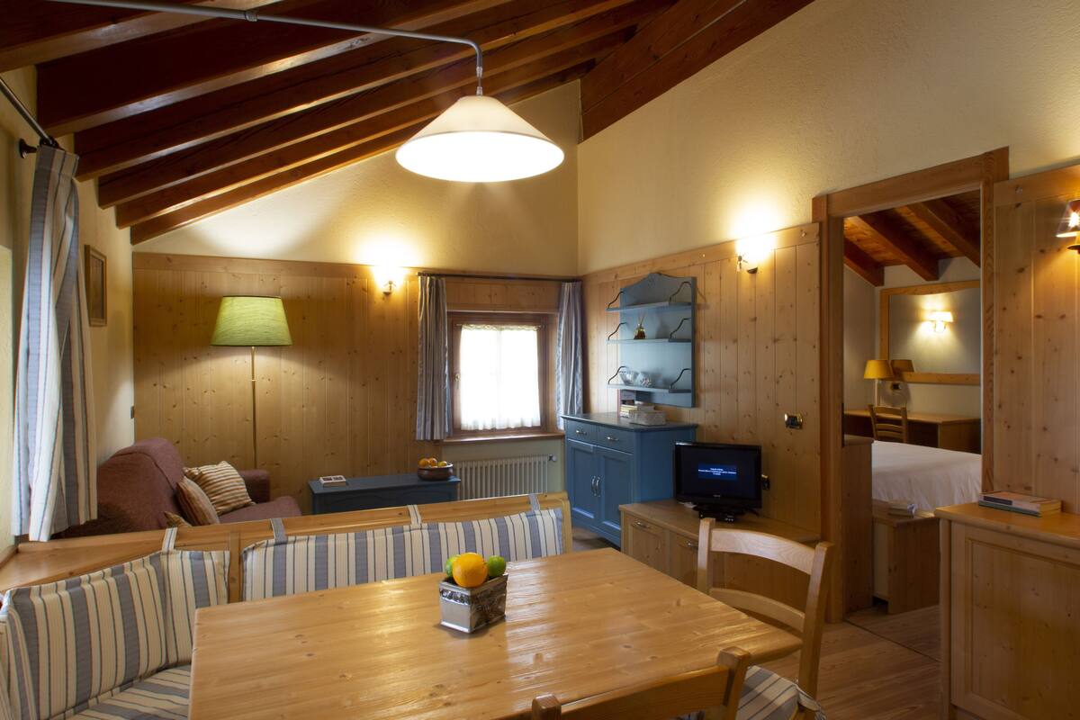 Un interior acogedor de cabaña con una mesa de comedor de madera, un sofá, un televisor y una zona de cocina.