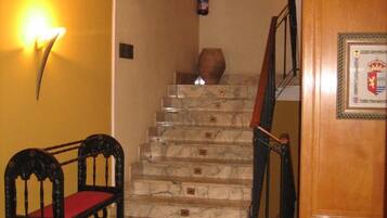 Un escalier avec des marches en marbre et une rampe en bois, menant à un palier orné d’un emblème encadré.
