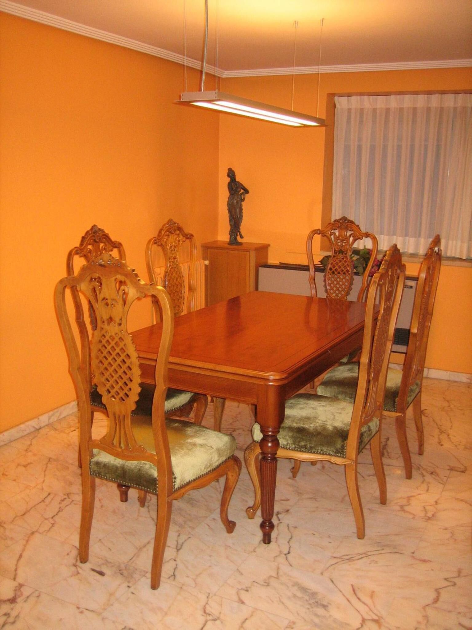 A dining room with a wooden table and chairs, a small statue, and a hanging light fixture.