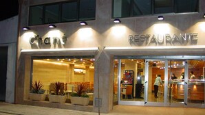 Restaurant amb façana de vidre, terrassa amb plantes en testos i interior visible amb taules i cadires.