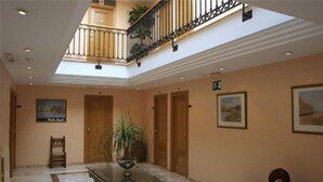 Un rebedor ampli amb un sostre alt, una taula central amb un ram i vistes a un balcó.