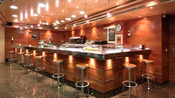 Zona de bar amb un taulell llarg, diverses solles i il·luminació penjant.