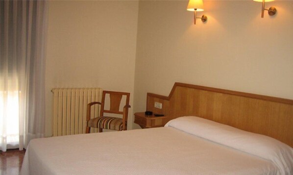 Une chambre d’hôtel comprenant un lit, une chaise, une table de chevet et deux lampes fixées au mur.