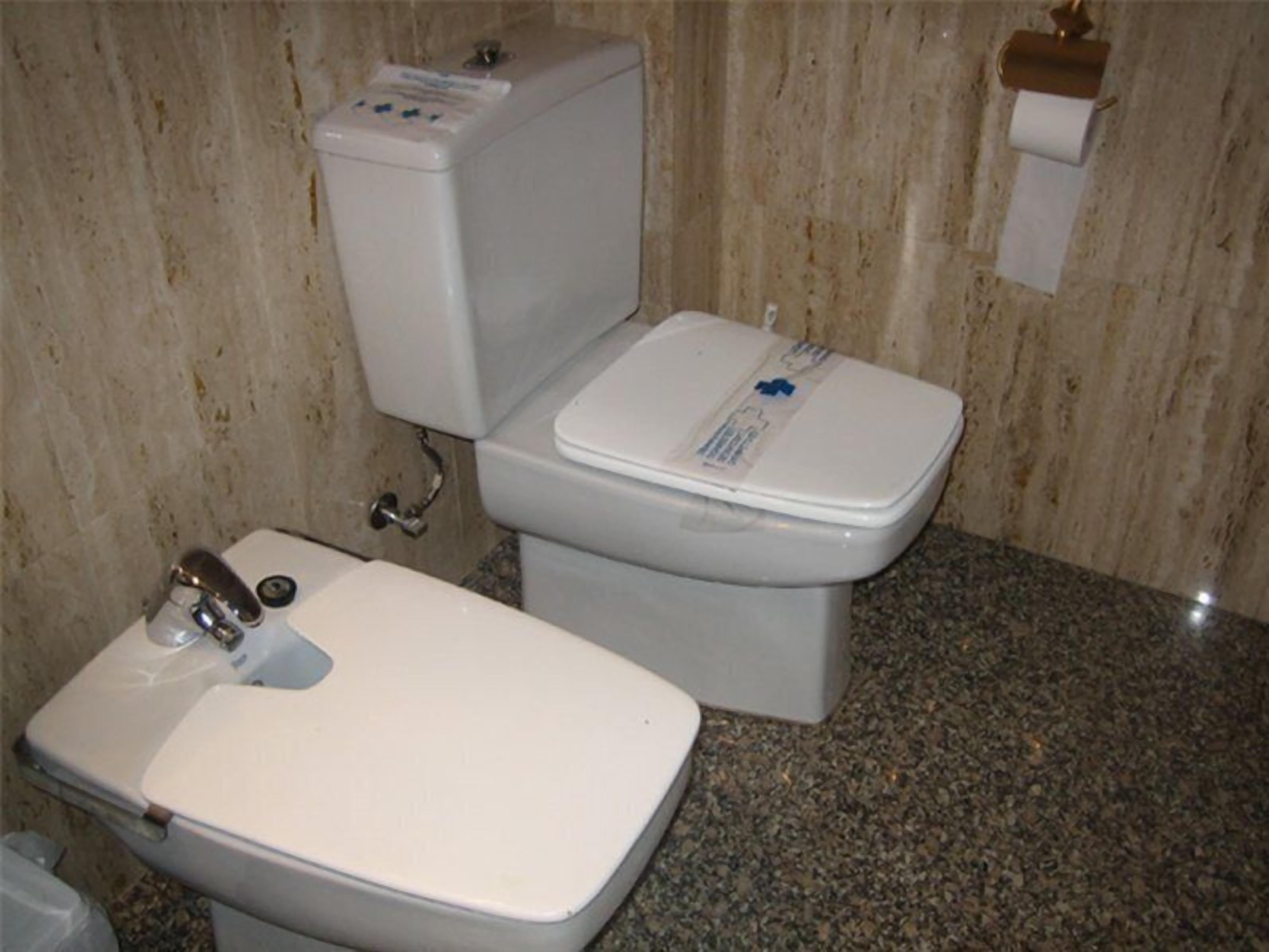 Un baño con inodoro, lavamanos y paredes de mármol.