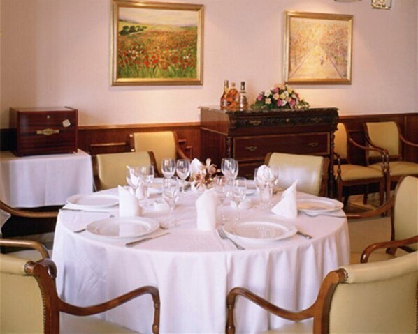 Un comedor con mesas redondas dispuestas para una comida, sillas de madera y cuadros en las paredes.