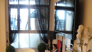 Een moderne badkamer met een groot, wit ligbad, een wandgemonteerde televisie en een houten vloer.