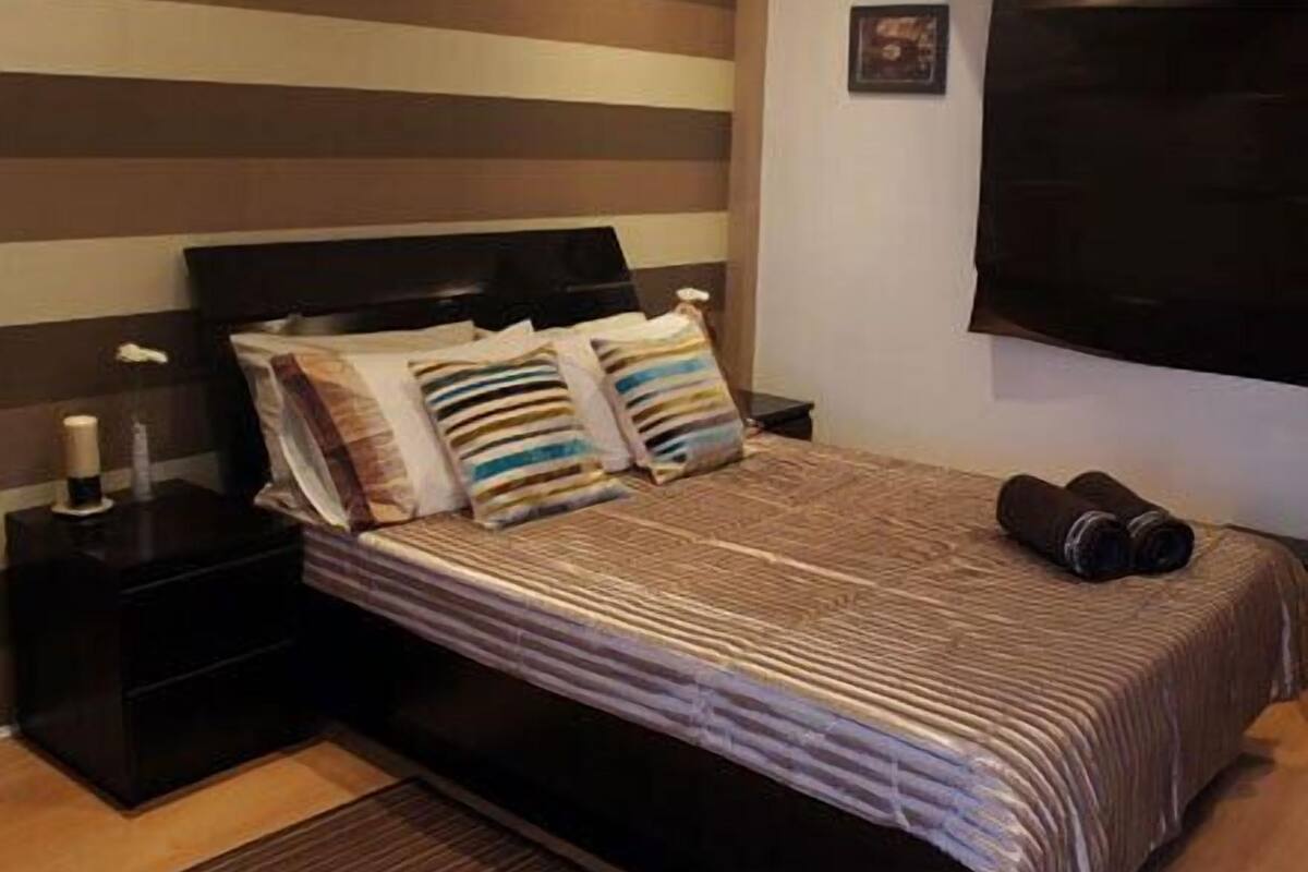 A neatly made bed with striped bedding, a dark headboard, and a pair of rolled-up towels on the side.