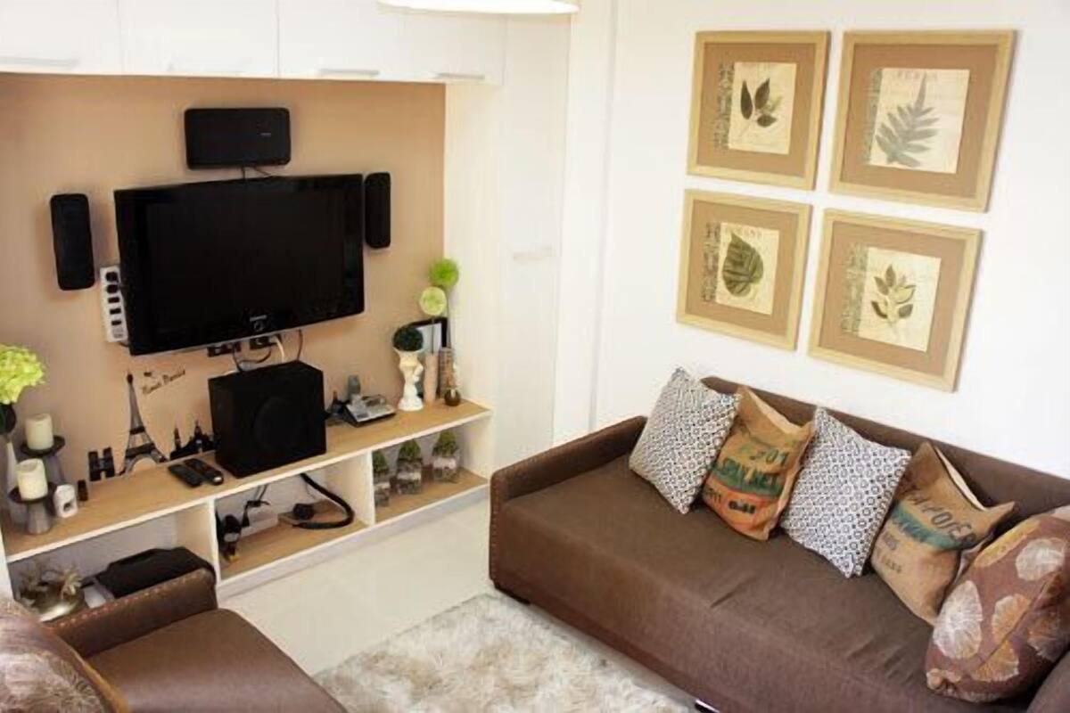 A living room with a flat-screen TV, a brown sofa, and framed botanical prints on the wall.
