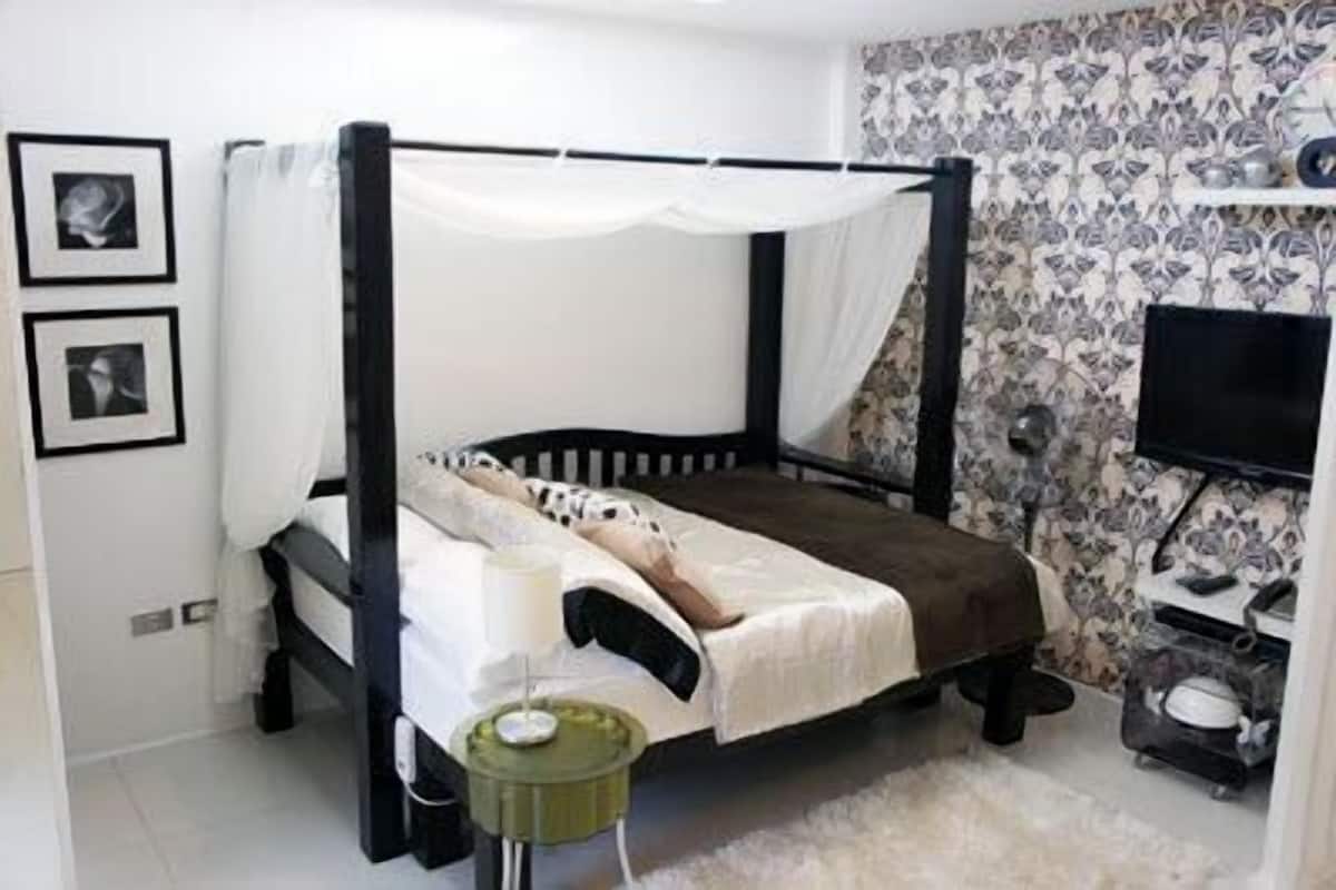 A single bed with a canopy, a bedside table with a lamp, and a television on a stand.