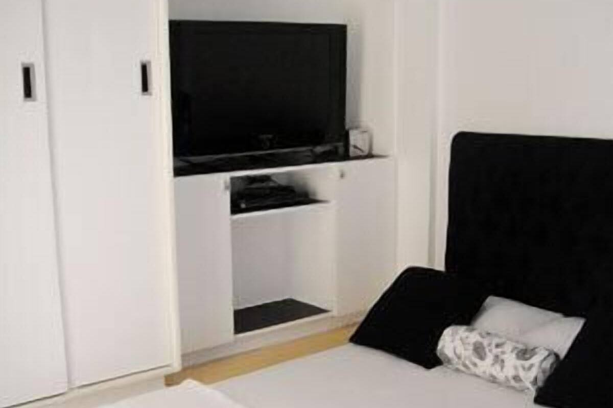 A bedroom with a bed, a TV, and a white wardrobe.
