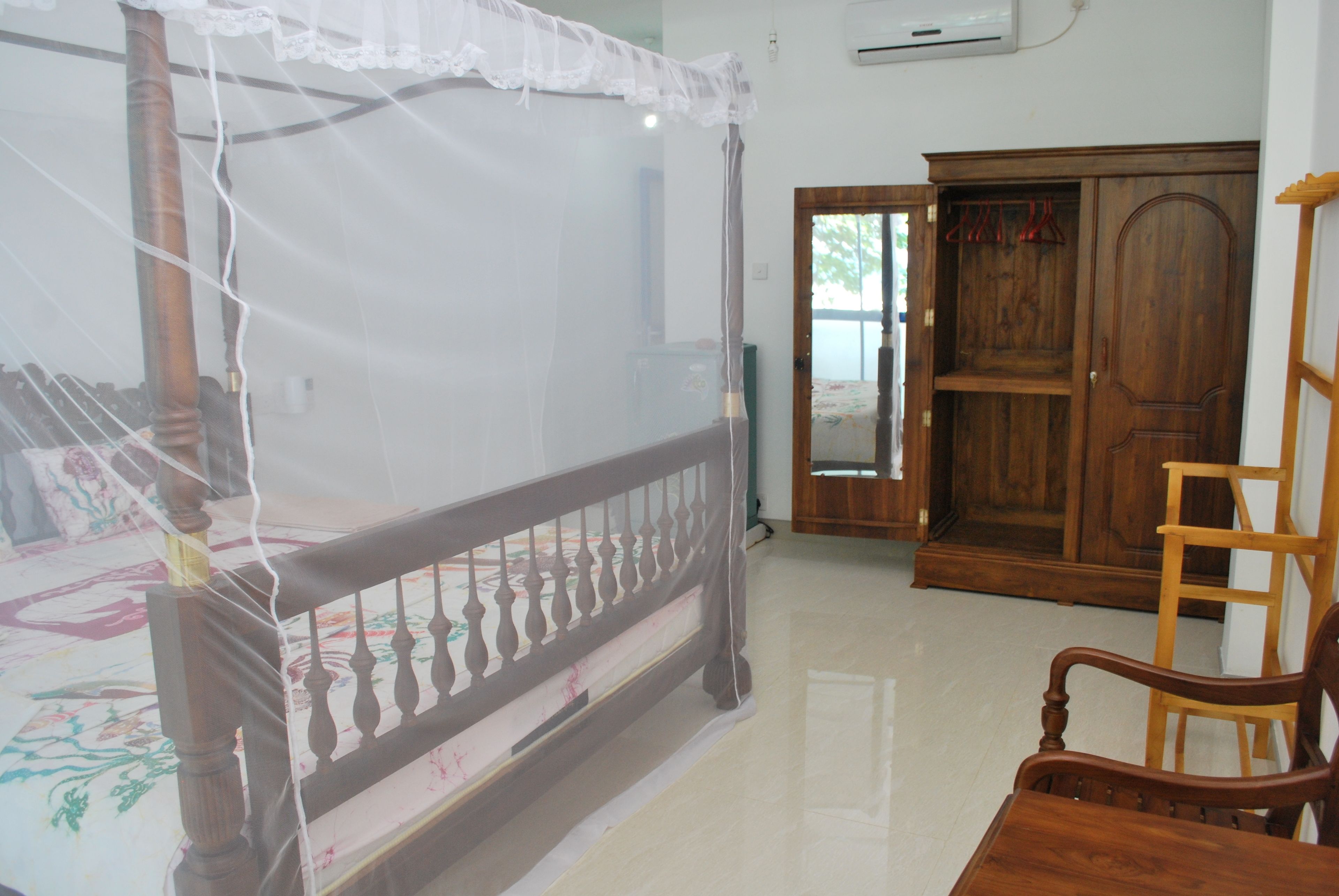 A room with a four-poster bed, a wooden wardrobe, and a wooden chair.