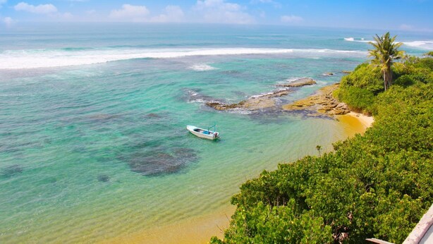 A coastal view with clear turquoise waters, a small boat, and lush greenery. - Paradise Beach Resort (Thalaramba)