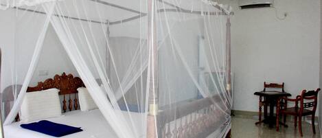 A room with a four-poster bed covered by a white canopy, a wooden headboard, a blue blanket, and a small table with chairs.