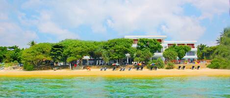 A beachfront hotel with a sandy beach, rows of sun loungers, and a clear view of the ocean.