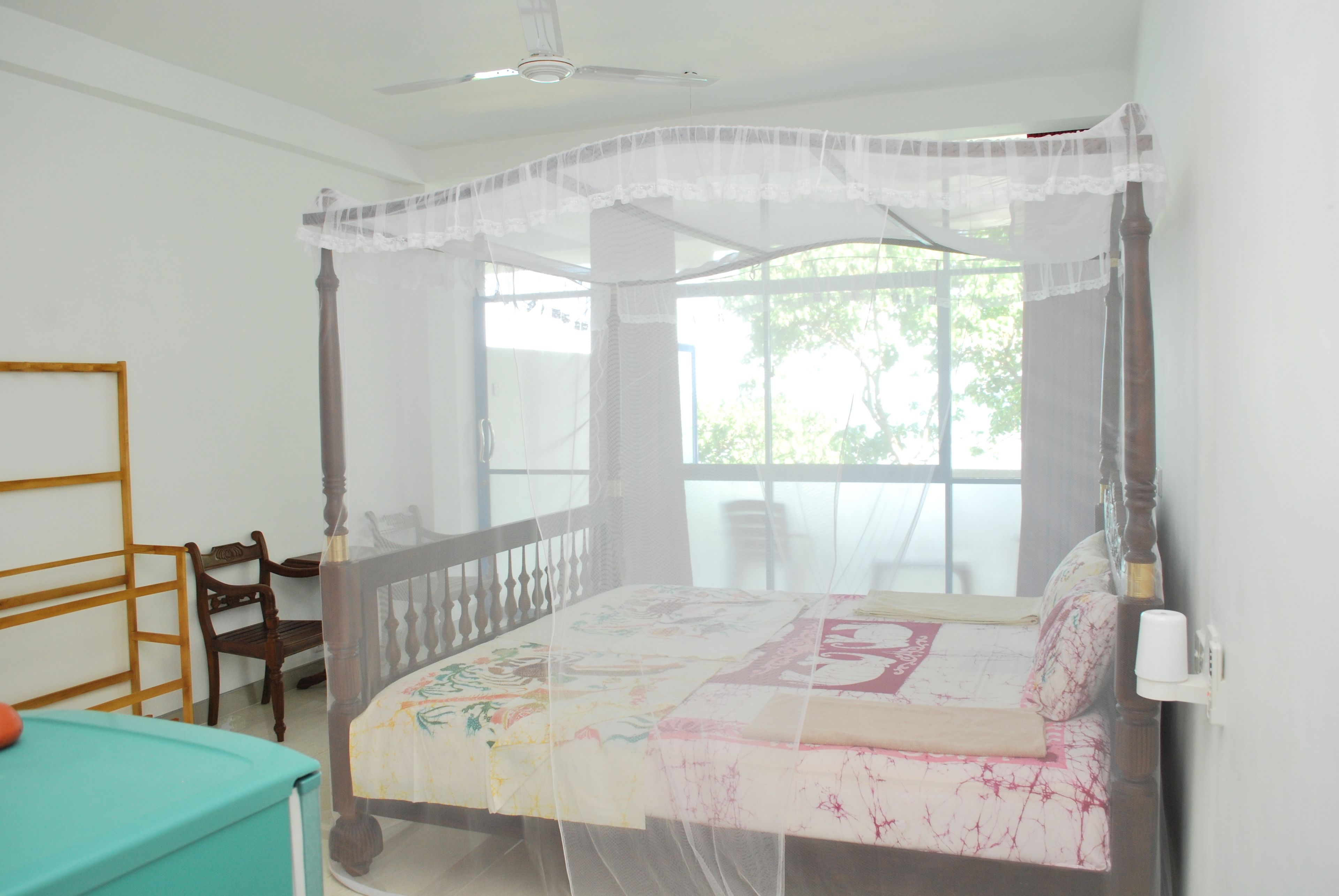Un dormitorio con una cama con dosel, una silla de madera y una ventana con vistas a árboles.