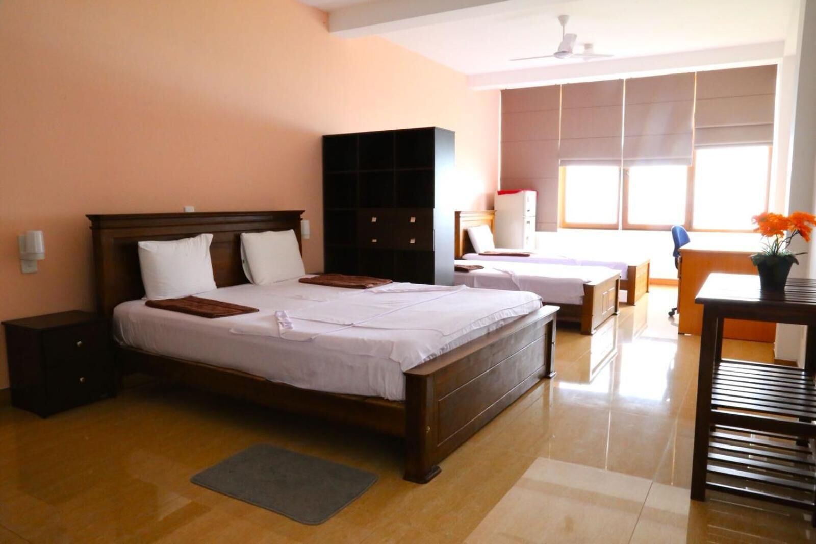 Quarto de hotel com duas camas, uma escrivaninha, uma cadeira, um guarda-roupa e uma janela com persianas.