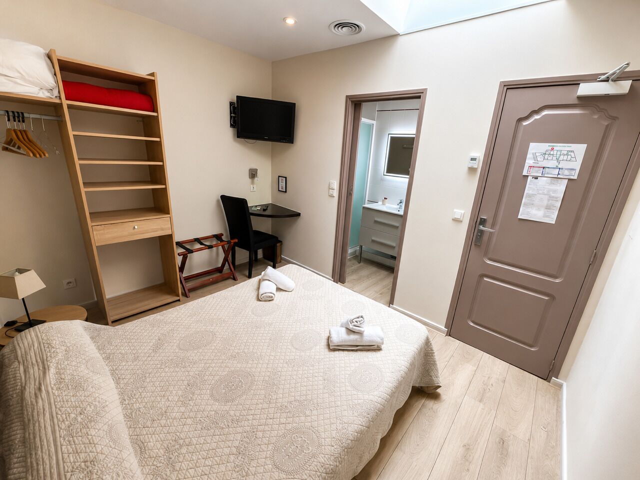 A bedroom with a bed, a desk, a chair, a wardrobe, a television, and a door with a notice.
