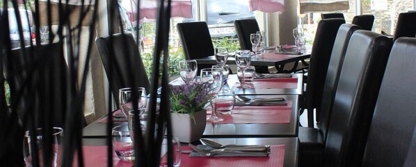 A dining area with tables set for two, chairs, and a potted plant on the table.