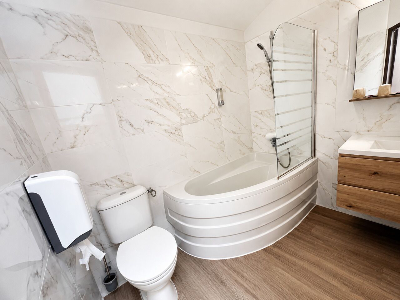 A modern bathroom with a marble wall, a freestanding bathtub, a toilet, and a wooden vanity.