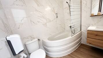 A modern bathroom with a marble wall, a freestanding bathtub, a toilet, and a wooden vanity.