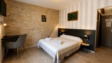 A hotel room with a bed, a desk, a chair, a nightstand, and a door.