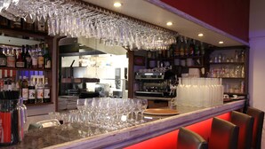 Zona de bar con mostrador, estantes llenos de botellas y una variedad de copas.