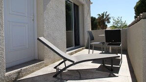 Un patio con una mesa, dos sillas, una puerta corrediza de vidrio y una pared exterior blanca.