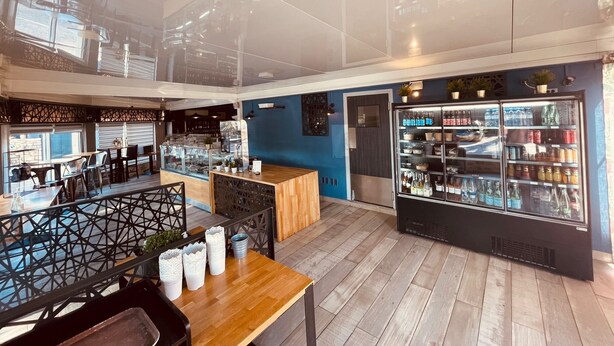 Un restaurante moderno con una mesa y sillas de madera, una barra y un refrigerador con bebidas.