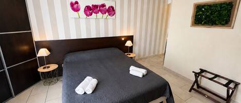 A hotel room with a large bed, two bedside tables, a headboard, a wall-mounted artwork of flowers, and a small bench.