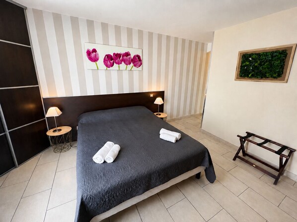 A hotel room with a large bed, two bedside tables, a headboard, a wall-mounted artwork of flowers, and a small bench.