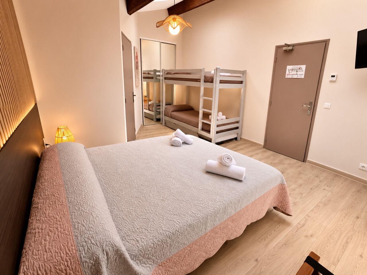 A hotel room with a large bed, a bunk bed, a bedside lamp, and a door with a sign.