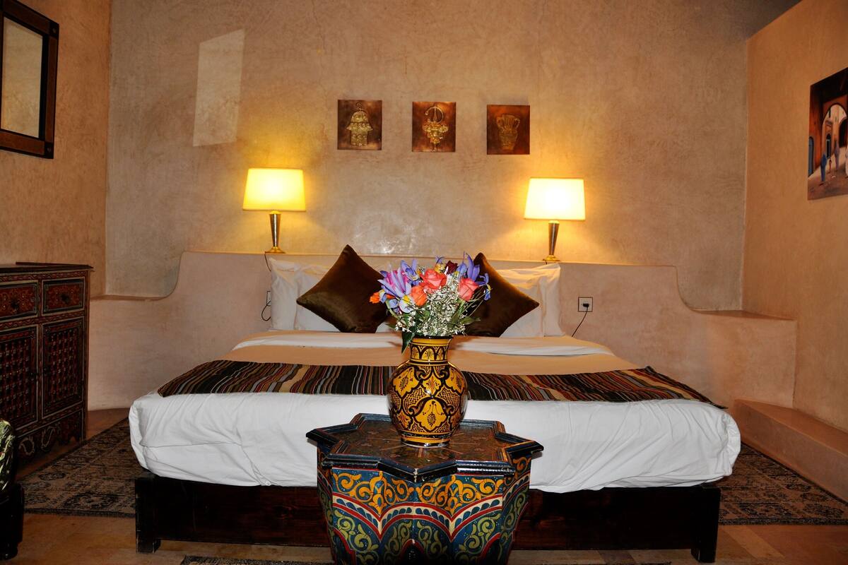 A hotel room with a large bed, two bedside lamps, a decorative vase, and a small table.