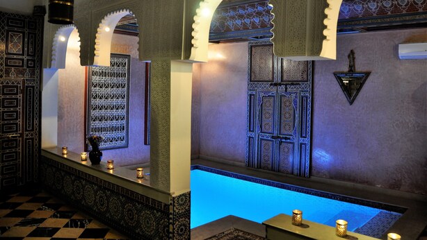 Une salle de bain luxueuse, ornée de motifs complexes en mosaïque, agrémentée d’une arche décorative et dotée d’un petit espace piscine.