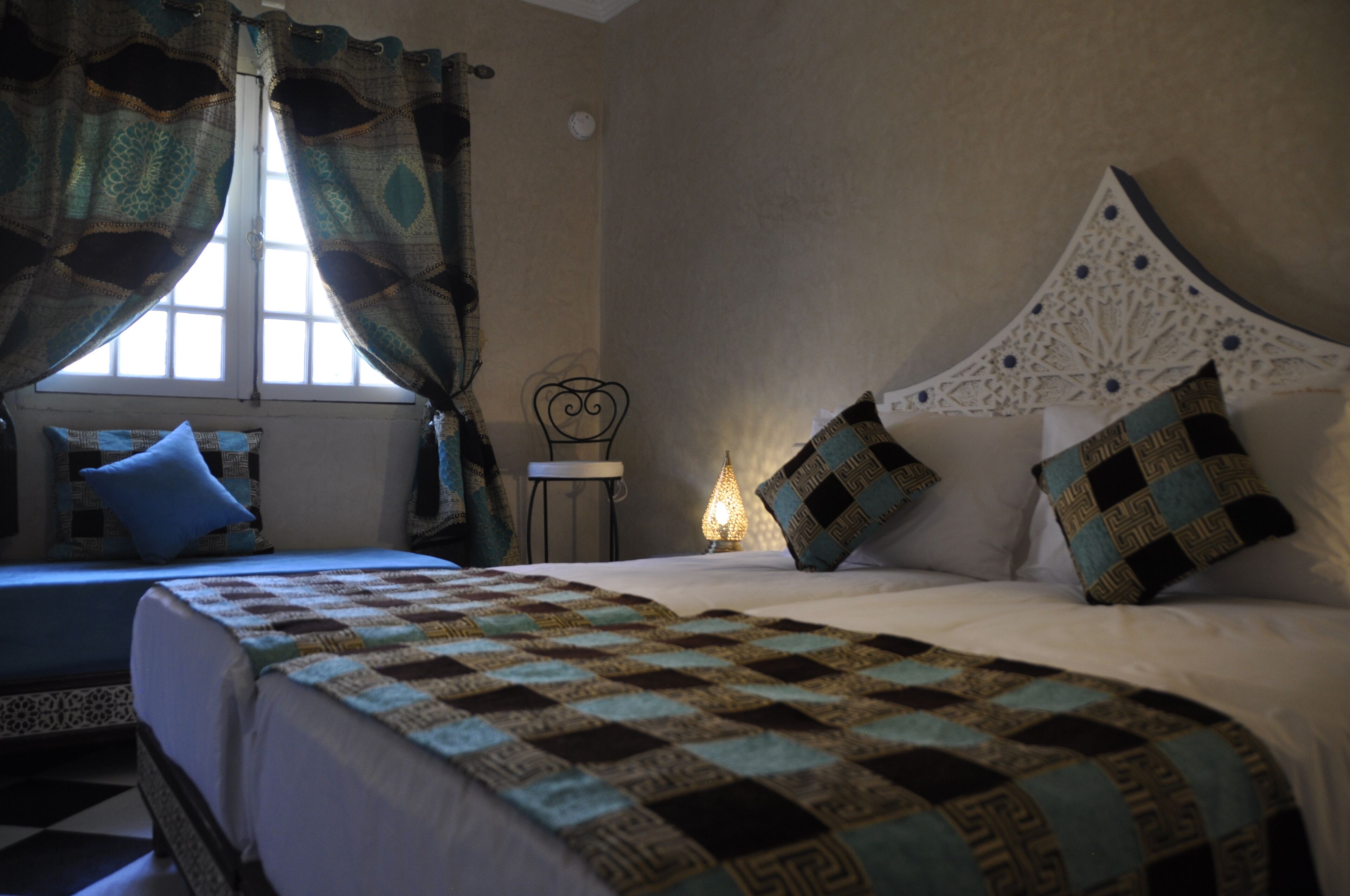 A bedroom with two beds, a nightstand, and a window with curtains.