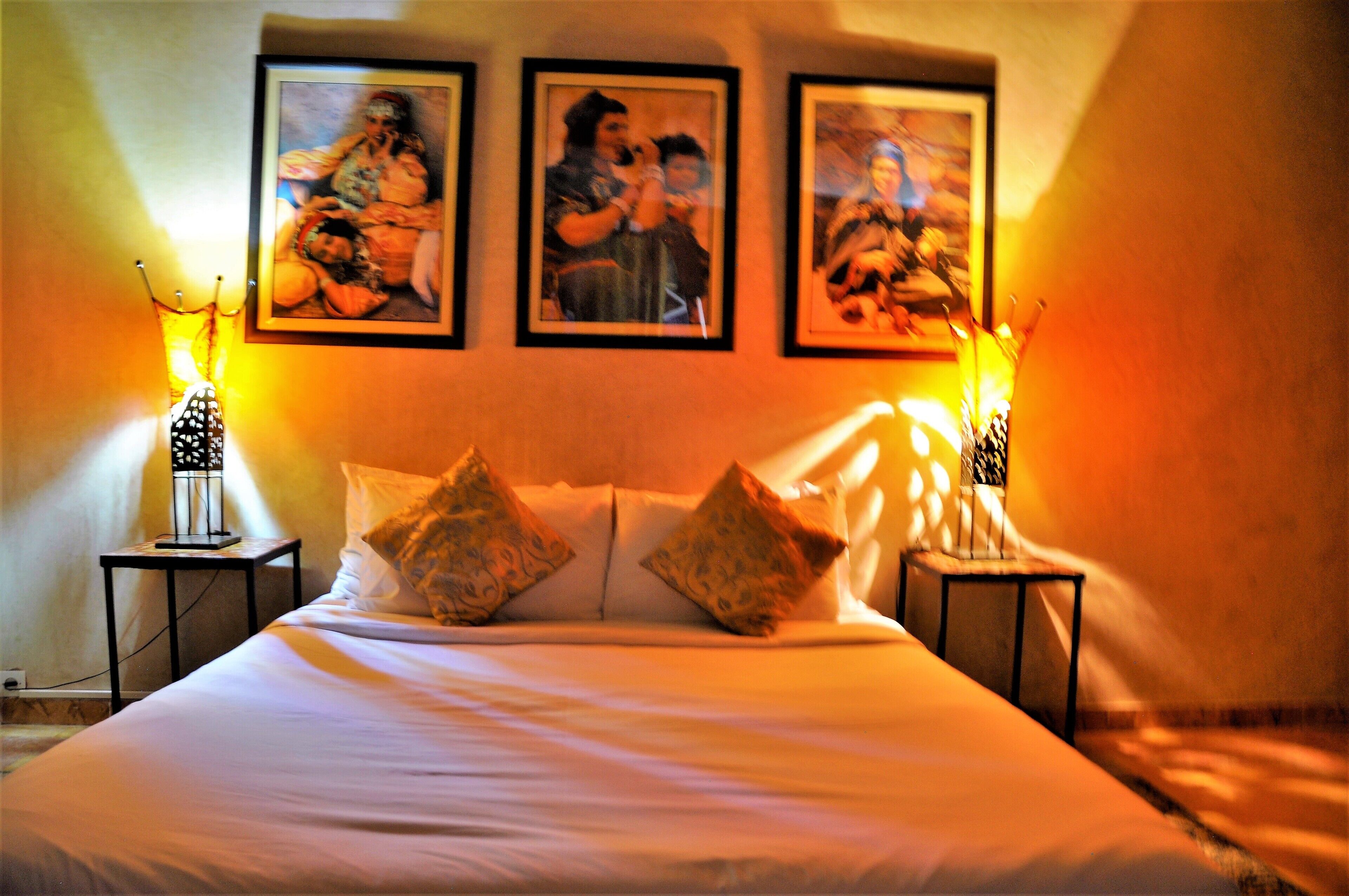 Une chambre d’hôtel avec un grand lit, deux tables de chevet et trois tableaux encadrés accrochés au mur.