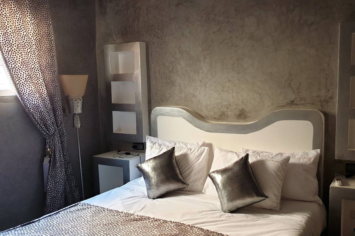 A bedroom with a bed, two nightstands, a lamp, and a patterned curtain.