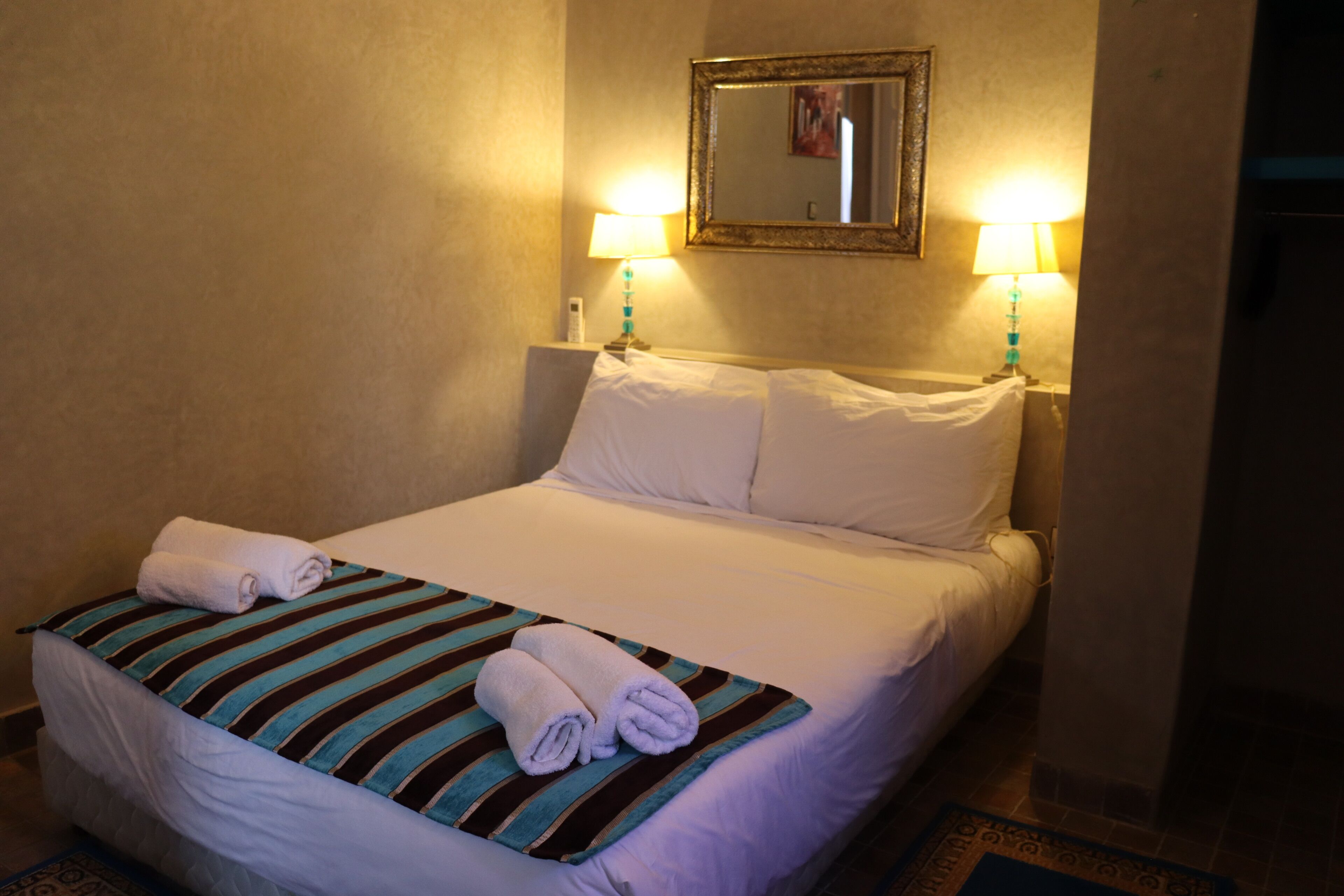 A hotel room with a neatly made bed, two bedside lamps, and a mirror on the wall.