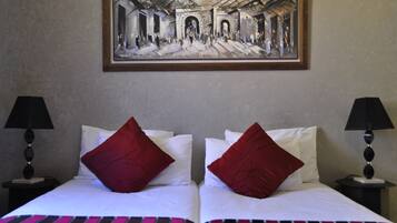 Une chambre d’hôtel avec deux lits, chacun agrémenté de draps blancs et d’oreillers rouges, un tableau encadré au-dessus des lits et deux lampes de chevet.