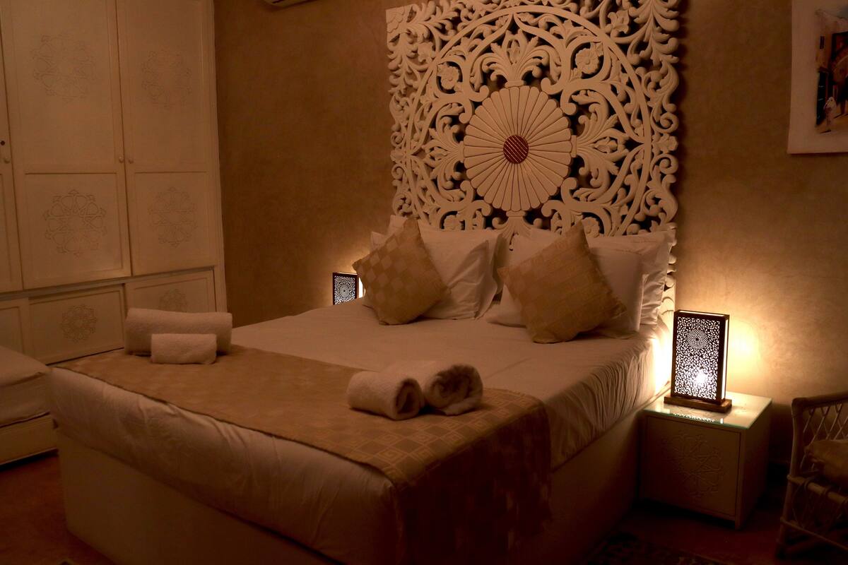A neatly made bed with a decorative headboard, a bedside table with a lamp, and a wall with a patterned design.
