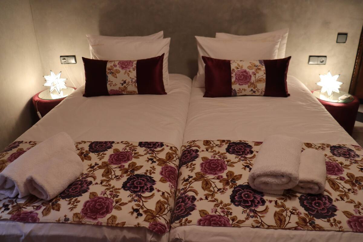 A double bed with floral bedding, two bedside tables with lamps, and a wall socket.